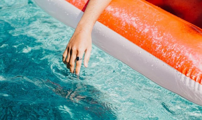 woman dangles her hand in the pool as she floats in an inflatable vessel
